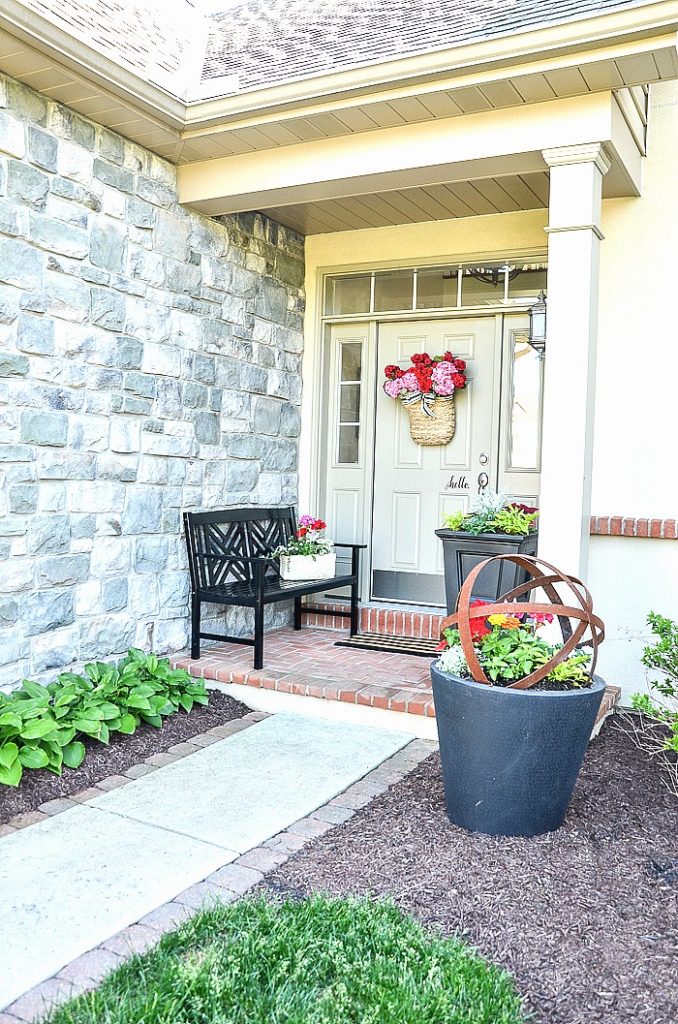 FRONT PORCH WITH BLACK BENCH AND PLANTERS WITH FLOWERS