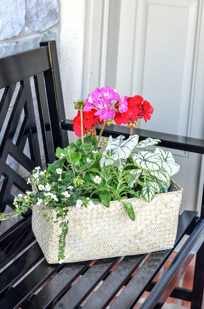  A BASKET OF FLOWERS ON A BENCH ON THE FRONT PORCH.