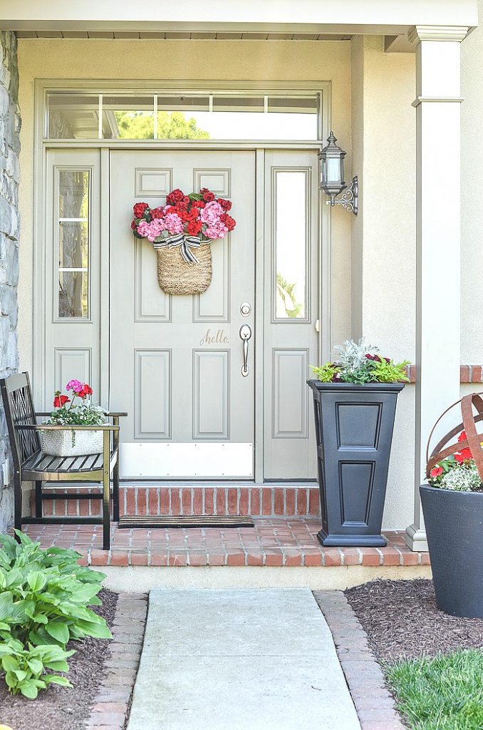 FRONT PORCH WITH BLACK BENCH AND PLANTERS FILLED WITH SUMMER FLOWERS