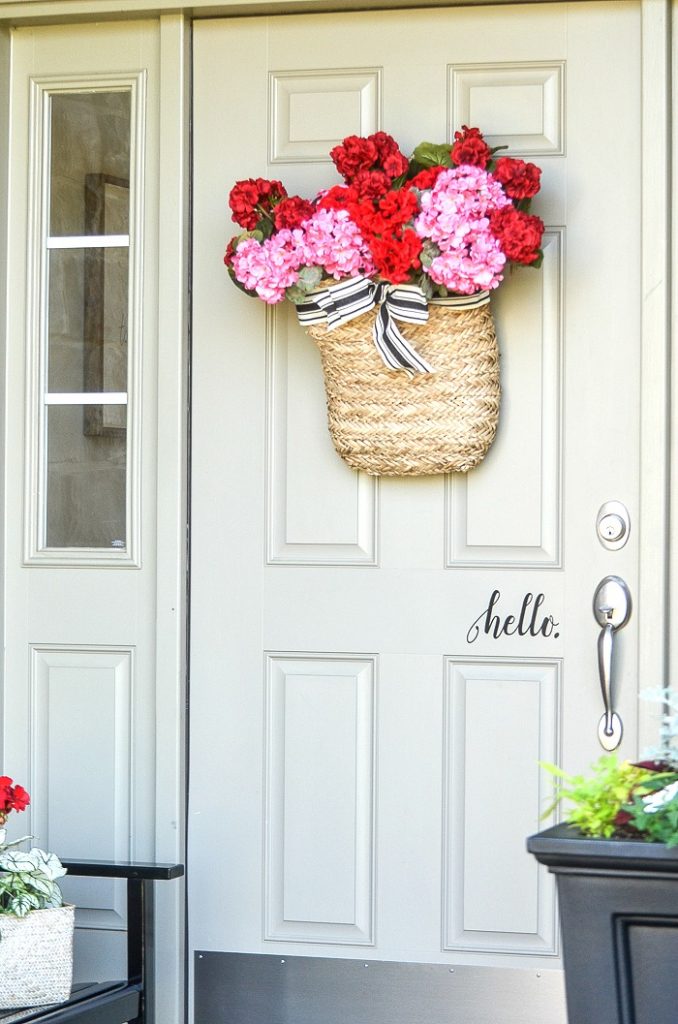 FRONT DOOR WITH A BASKET OF RED AND PINK GERANIUMS ON IT.