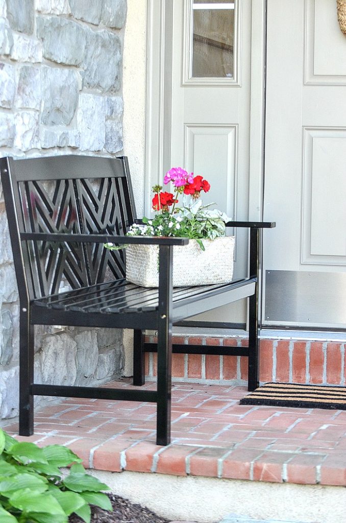 BENCH ON A SMALL FRONT PORCH WITH A BASKET OF FLOWERS SITTING ON IT