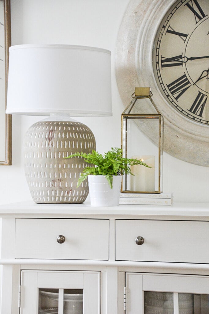 a lantern on a white buffet with a small fern plant