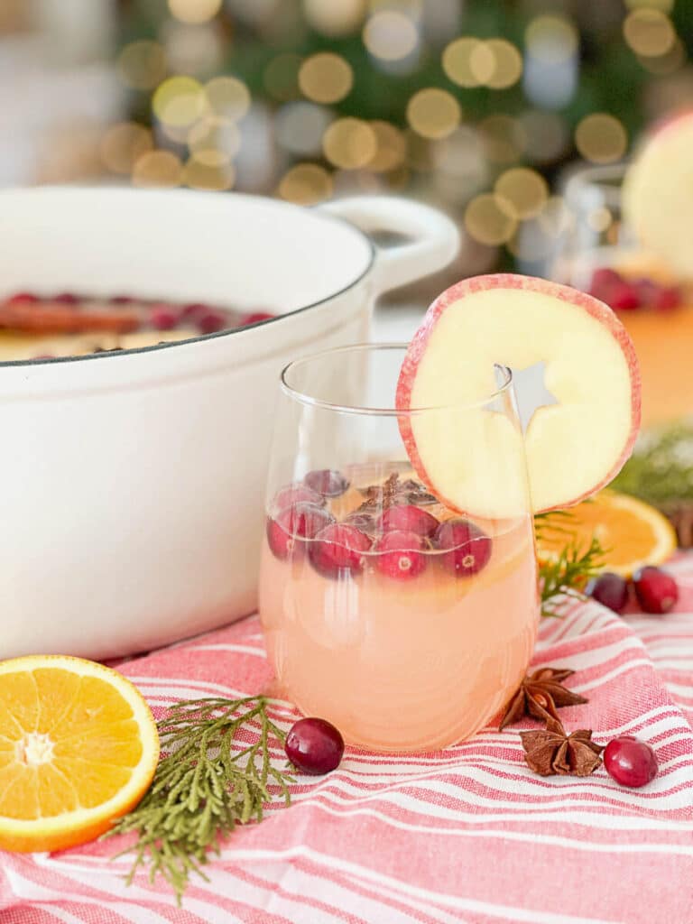 glass of mulled cider with a pot of cider in the background