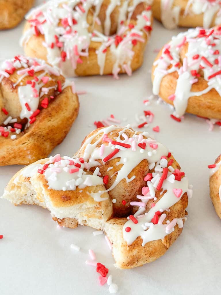 heart shaped cinnamon rolls, one with a bite out of it.